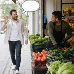 A passerby waves and speaks to a man working at a greengrocer stand, with an empty oval speech bubble from the passerby.