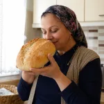 A woman smells a fresh loaf of bread in a kitchen.