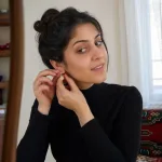 An adult woman fastening an earring, with the earring as the visual focus.