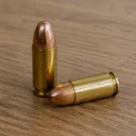 Inert brass cartridges arranged on a wooden table with no firearm present.