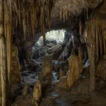 A view from inside a cave with stalactites hanging above and stalagmites rising from the floor.