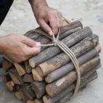 Close photo of hands tying a bundle of firewood with rope.