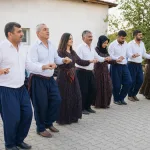 Group of adults holding hands in a line dance outdoors.